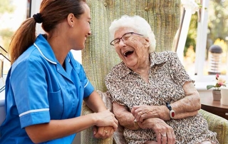 Senior Woman Sitting In Chair And Laughing With Home Healthcare Agency