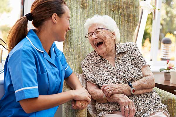 Senior Woman Sitting In Chair And Laughing With Home Healthcare Agency