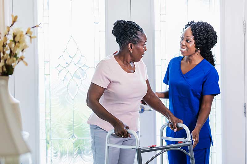 healthcare worker visiting a senior woman at home helping her use a mobility walker