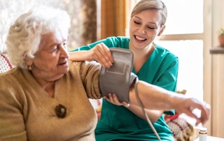 Female caretaker measuring senior woman's blood pressure at home