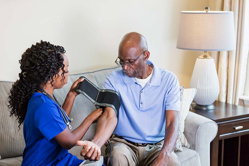 A healthcare worker visiting a senior African-American man in his home, checking his blood pressure