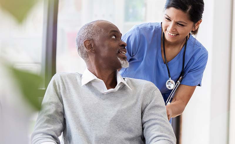 senior man sits in a wheelchair smiling back at a home health aide